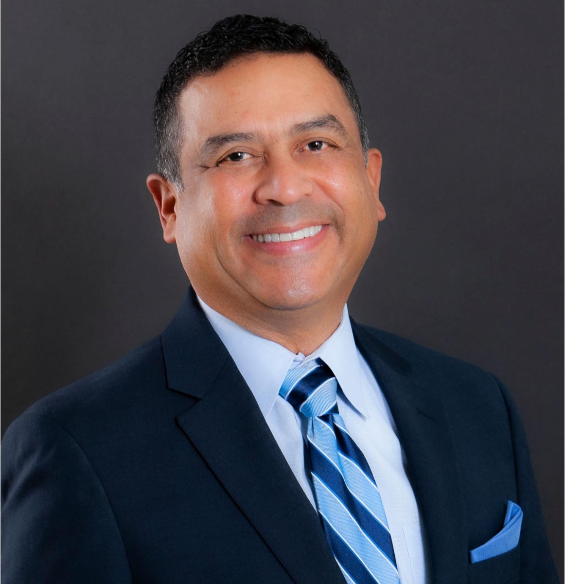 The image shows two photographs side by side of a man wearing a suit with a tie, smiling at the camera, against a dark background.
