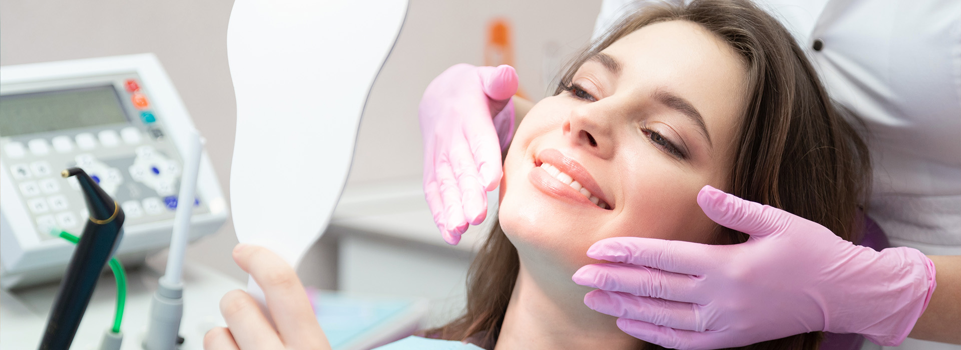 A woman receiving dental care with a hygienist, having her teeth cleaned under a magnifying lamp.