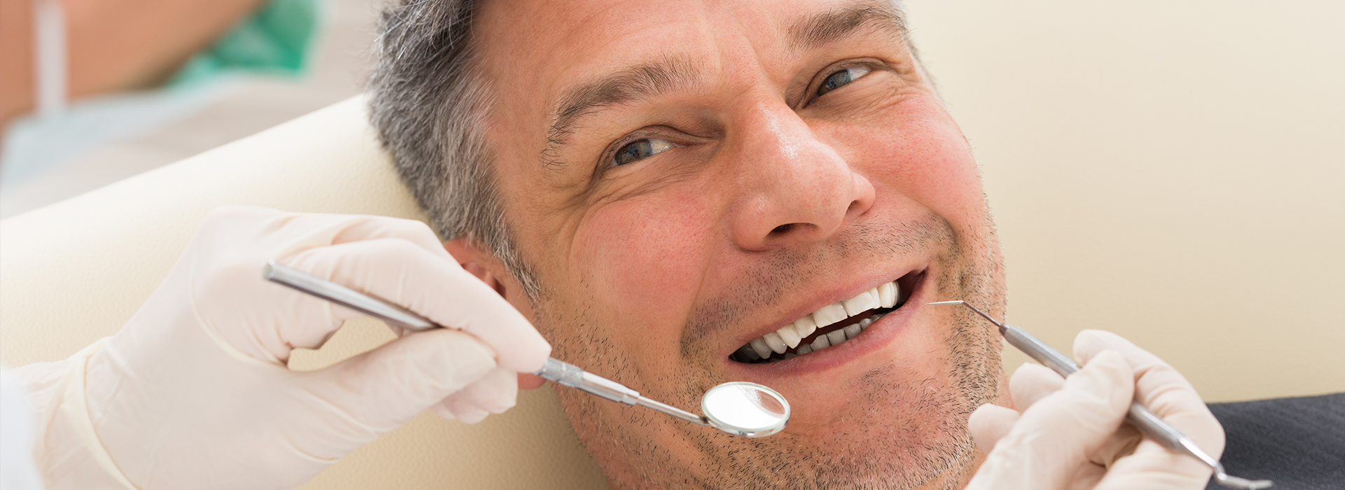 A man with a toothy grin receiving dental care from a dentist, surrounded by dental tools and equipment.