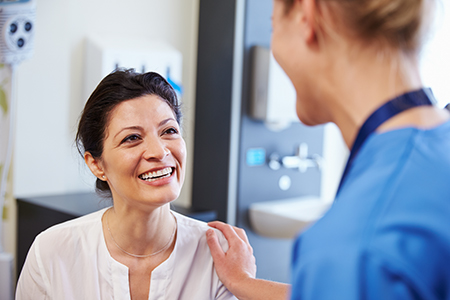 The image shows two individuals in a medical setting one appears to be a patient receiving care from a healthcare professional, with both smiling at each other.